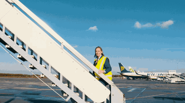 a woman in a yellow vest stands on a set of stairs in front of a ryanair airplane
