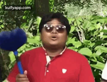 a man wearing sunglasses and a red shirt is holding a blue microphone and making a funny face .