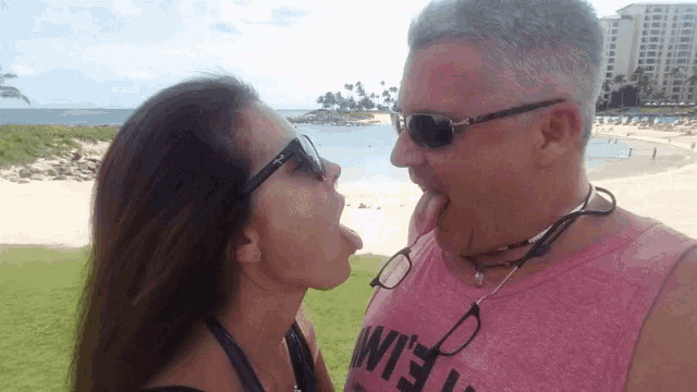 a man wearing a pink tank top with the word wife on it kisses a woman on the beach