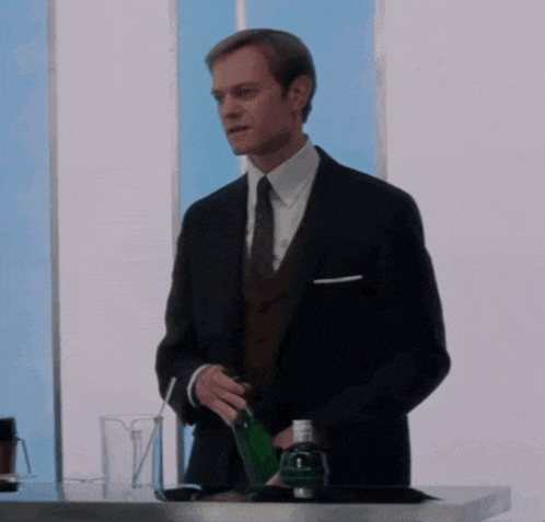 a man in a suit and tie holds a green bottle with the letter l on it