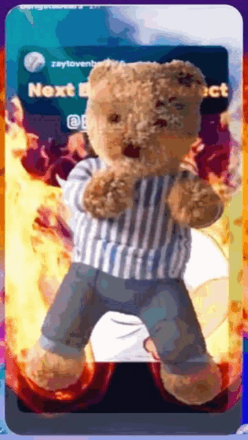 a teddy bear wearing a striped shirt and jeans is standing in front of fire
