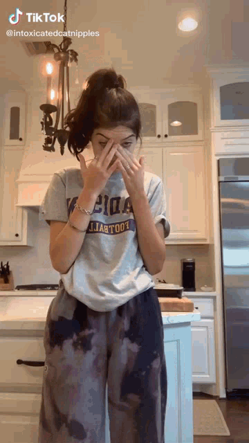 a woman wearing a t-shirt that says ' atlanta ' on it covering her face in a kitchen