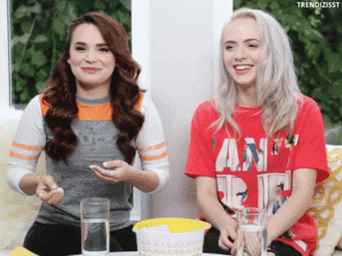 two women are sitting on a couch with one wearing a red shirt that says vanity fair