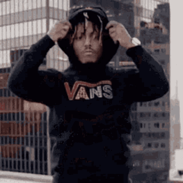 a man is wearing a black vans hoodie and adjusting his hood .