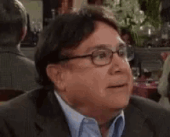 a man wearing glasses and a suit is sitting at a table in a crowded room .