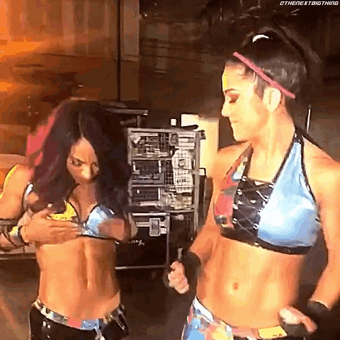 two female wrestlers are standing next to each other in a room and one of them is adjusting her bra .