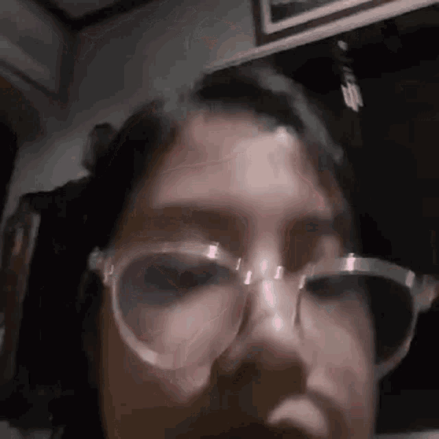 a woman wearing glasses is taking a selfie in a dark room .