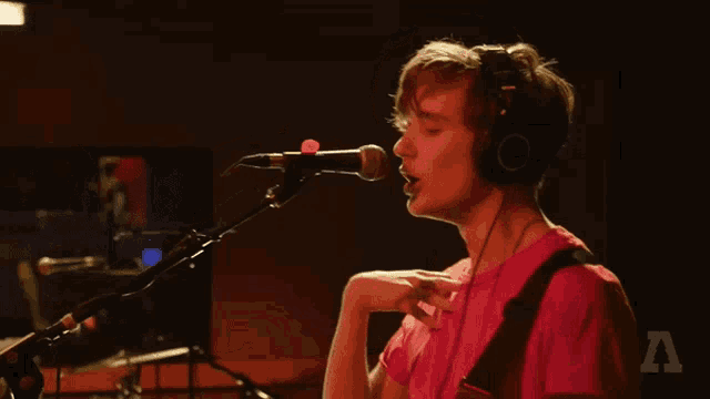 a man in a pink shirt is singing into a microphone while playing a guitar