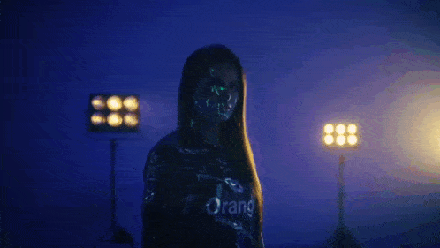 a woman in a black shirt is standing in front of a row of lights in a dark room .