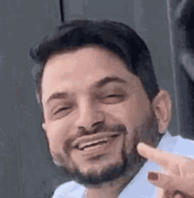a man with a beard is smiling and giving the peace sign .