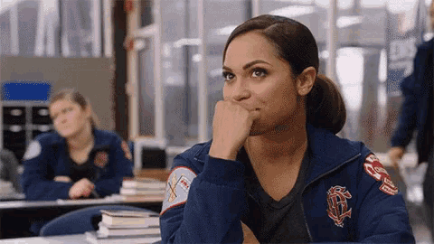 a woman in a firefighter 's uniform is sitting at a table with her hand on her chin .