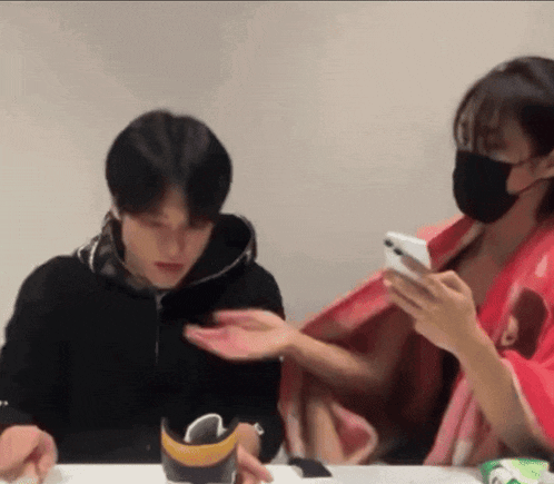 a man and a woman are sitting at a table looking at a phone