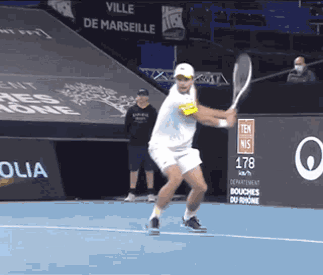 a man swings a tennis racquet on a tennis court in front of a sign that says " ville de marseille "
