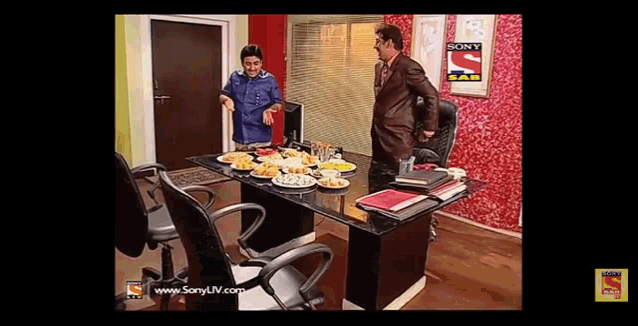 two men are sitting at a table with plates of food and a sony logo on the wall