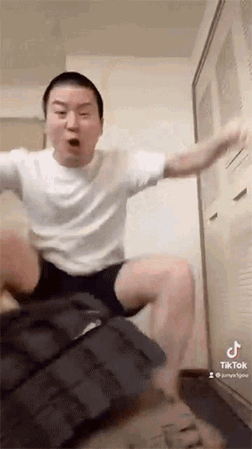 a man in a white shirt and shorts is sitting on a couch and making a funny face .