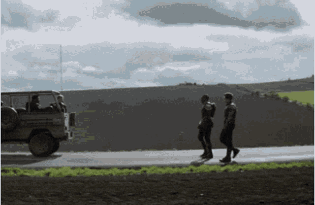 a group of people walking down a road with a truck behind them