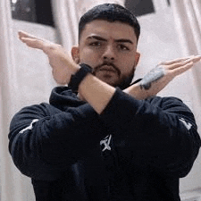 a man with a beard and a tattoo on his arm is making a funny face with his arms crossed .