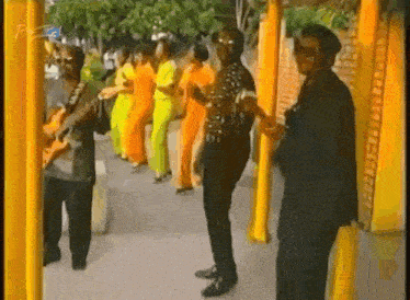 a man is playing a guitar in front of a group of people wearing yellow pants .