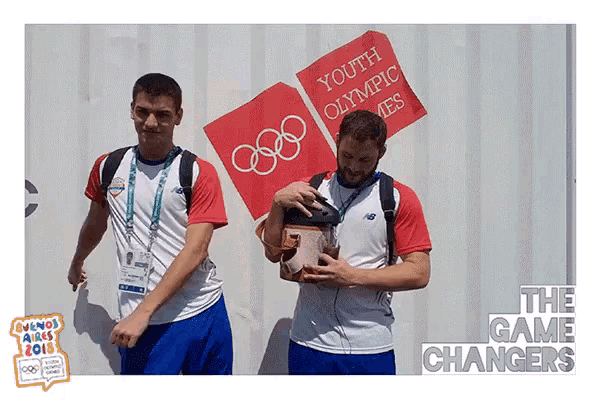 two men standing in front of a youth olympic games sign