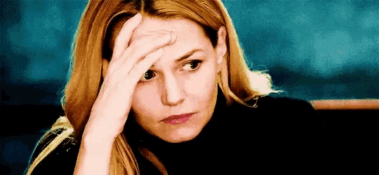 a woman is holding her head with her hand and looking at the camera .