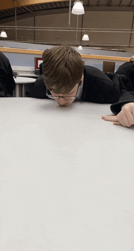 a boy with glasses laying on a table with his head down