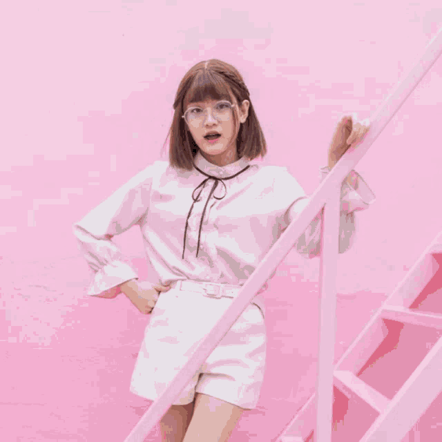a girl wearing glasses and a white shirt is standing next to a pink staircase