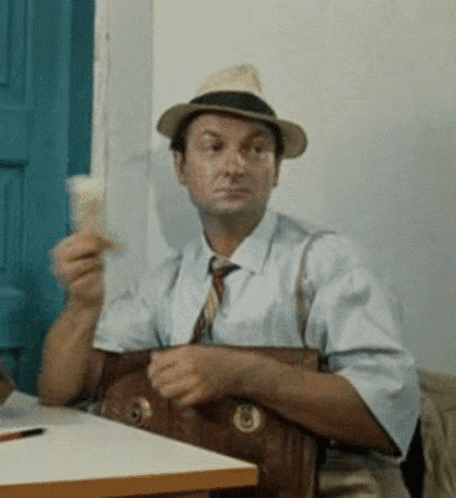 a man wearing a hat and tie is sitting at a table holding a purse