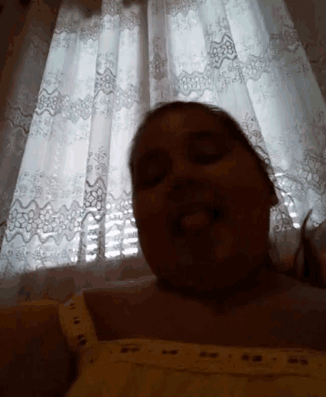 a woman is taking a selfie in front of a window with curtains .
