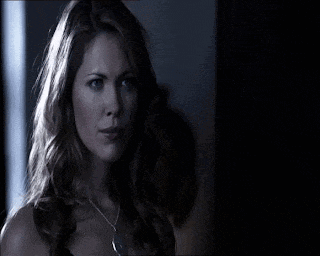 a woman with long hair is wearing a necklace and looking at the camera in a dark room .