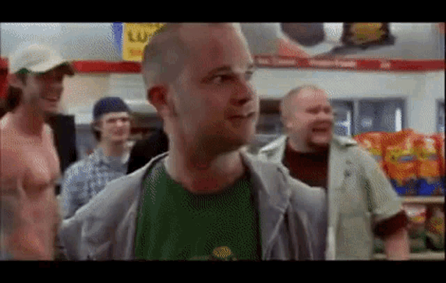 a bald man in a green shirt is standing in a store with other men .