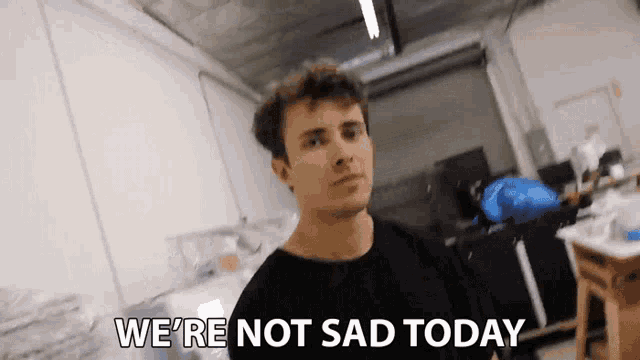 a man in a black shirt is standing in a room with the words `` we 're not sad today '' written on his face .