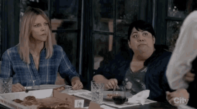 a group of women are sitting at a table with pizza boxes .