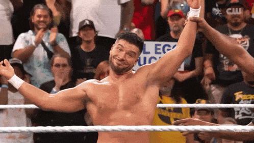 a shirtless wrestler in a wrestling ring with a crowd behind him and a sign that says college uc