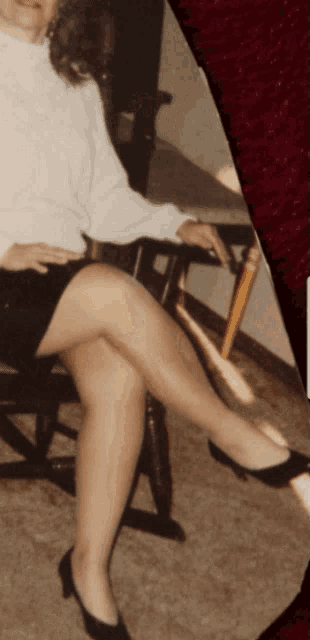 a woman in a white shirt and black skirt sits on a chair with her legs crossed