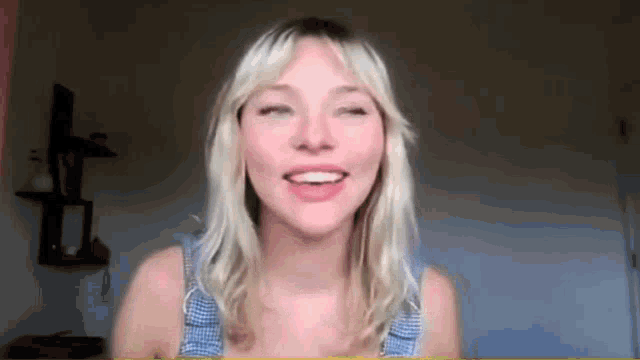 a woman with blonde hair is smiling and looking at the camera while wearing a blue tank top .