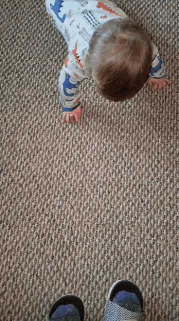 a baby crawling on a carpet with a dinosaur on his shirt