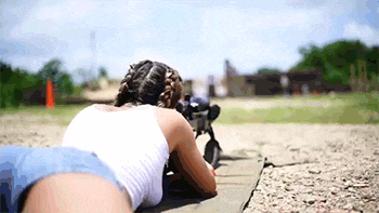 a woman is laying on the ground with a rifle .