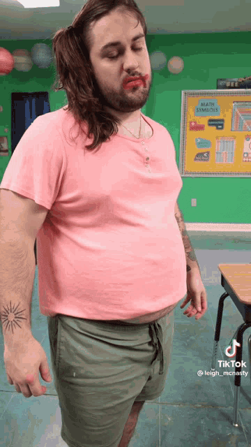 a man with long hair and a tattoo on his arm is wearing a pink shirt and green shorts