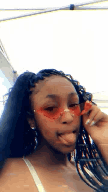 a young woman wearing red sunglasses is sticking out her tongue .