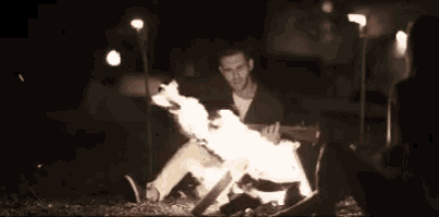 a man playing a guitar in front of a fire at night