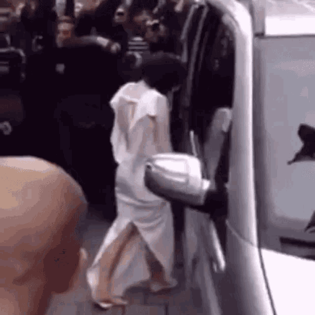 a woman in a white dress is walking towards a car .