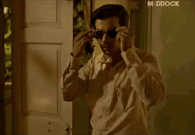 a man wearing sunglasses is standing in front of a door that says mddock on the bottom