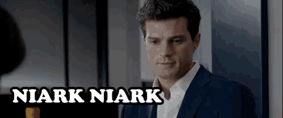 a man in a suit and white shirt is standing in front of a mirror with the name niark niark written above him .