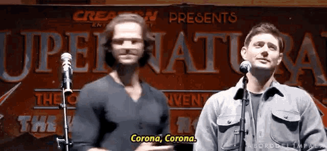 two men are standing in front of microphones in front of a sign that says supernatural .