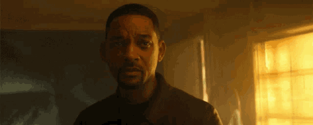 a man is standing in front of a window in a dark room and looking at the camera .