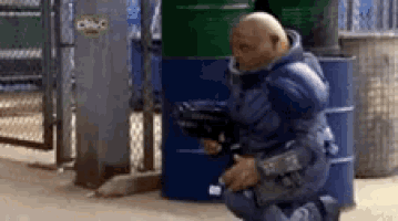 a man in a blue suit is kneeling down and holding a gun in a room .