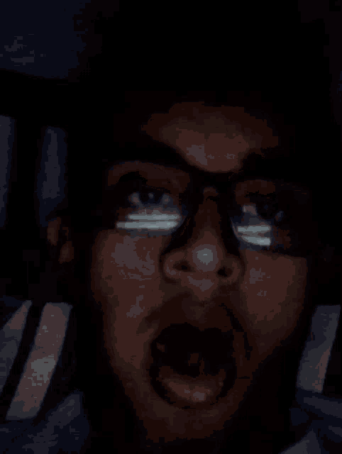 a man wearing glasses is making a funny face in the dark