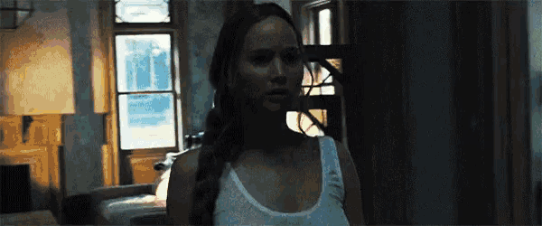 a woman in a white tank top is standing in a dark room with a window .