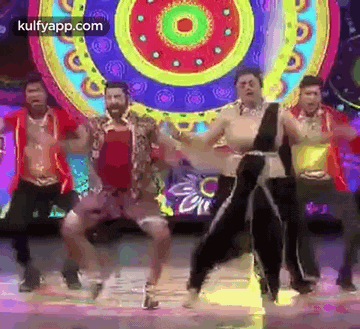 a group of men and women are dancing on a stage in front of a colorful background .