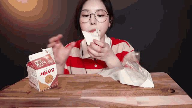 a woman is eating a sandwich next to a carton that says ' korean ' on it
